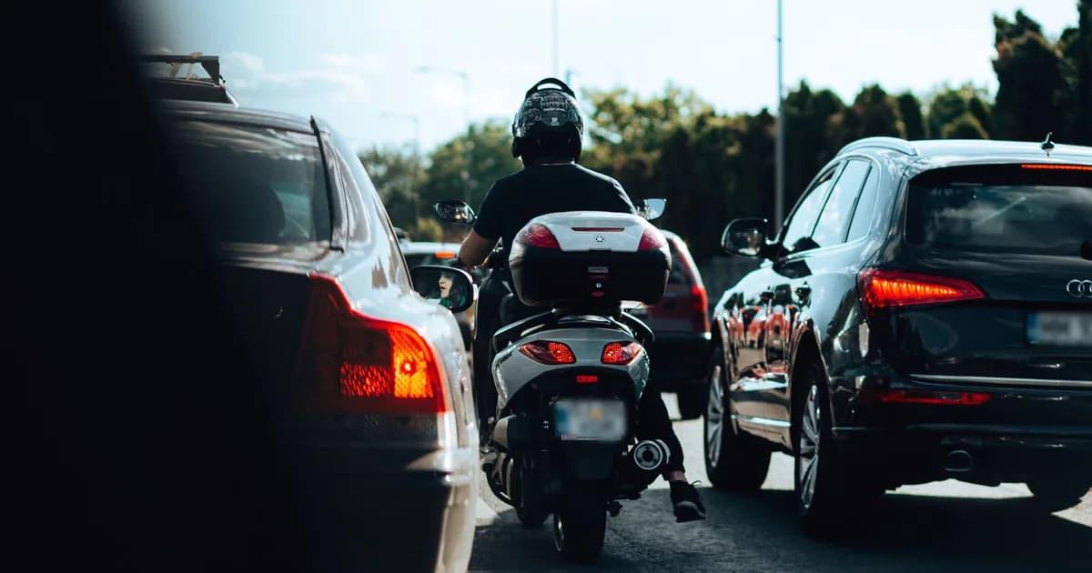 Scooter com baú passa entre duas filas de carros parados no congestionamento, vista traseira