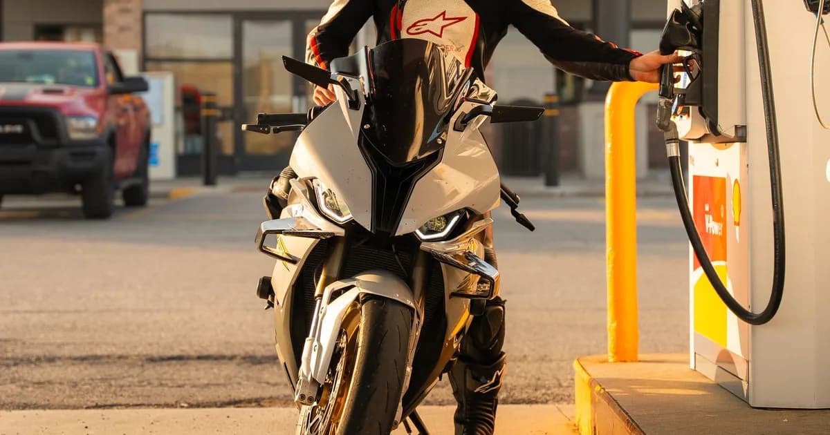 Motociclista abastece a moto na bomba de um posto, com a mão no bico de combustível