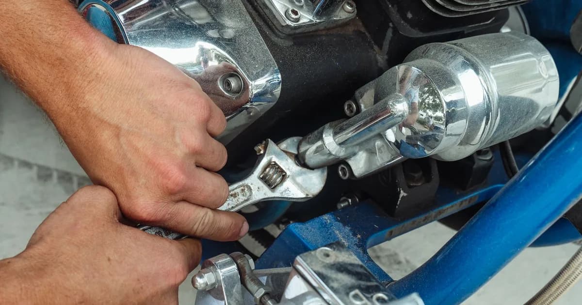 Mãos seguram uma chave ajustável sobre o motor de uma moto durante manutenção na garagem